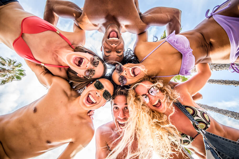 A group of college-aged friend form a circle, looking downwards to the camera, while celebrating spring break in Fort Lauderdale.